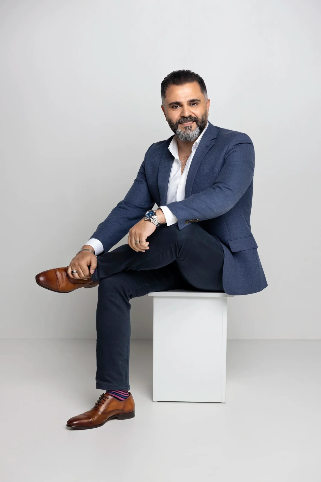 Alaa Hassan, founder of Red Goat Digital, seated in a navy suit against a light backdrop